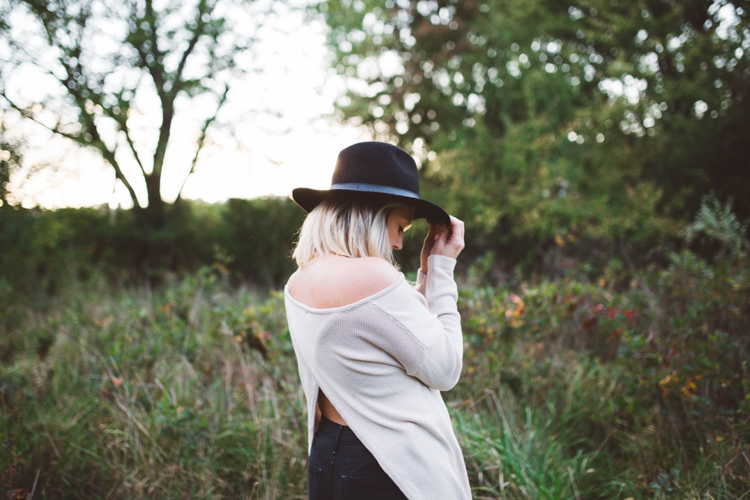 woman in white off shoulder long sleeved top holding black hat