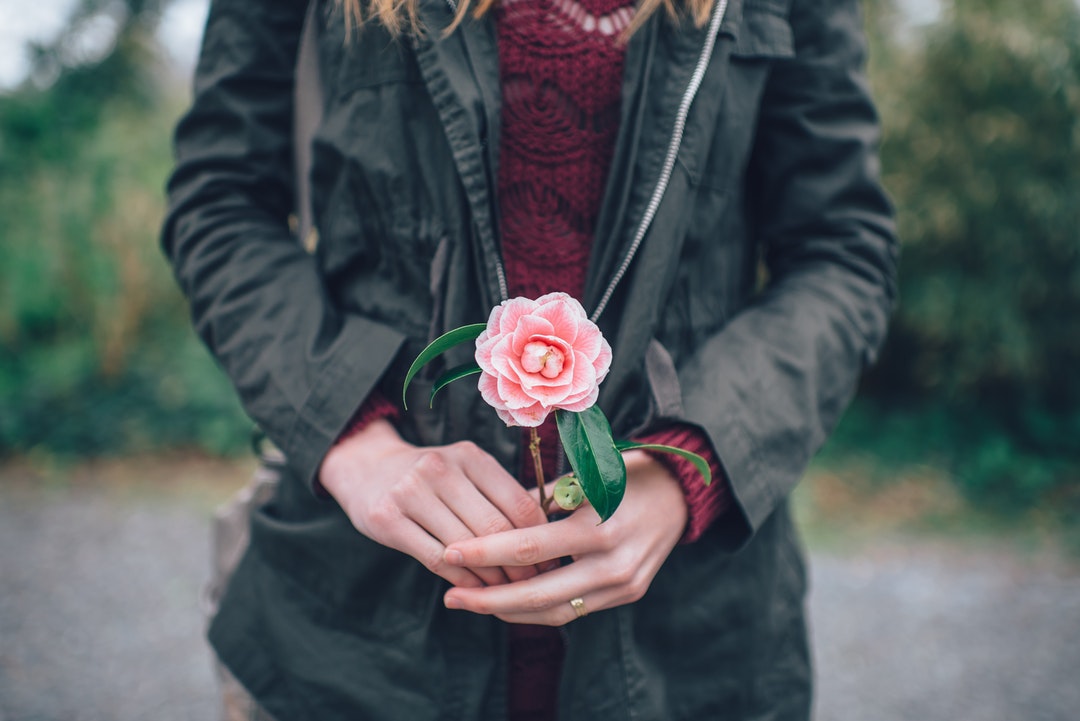 A woman in a jacket holding a small pink peony