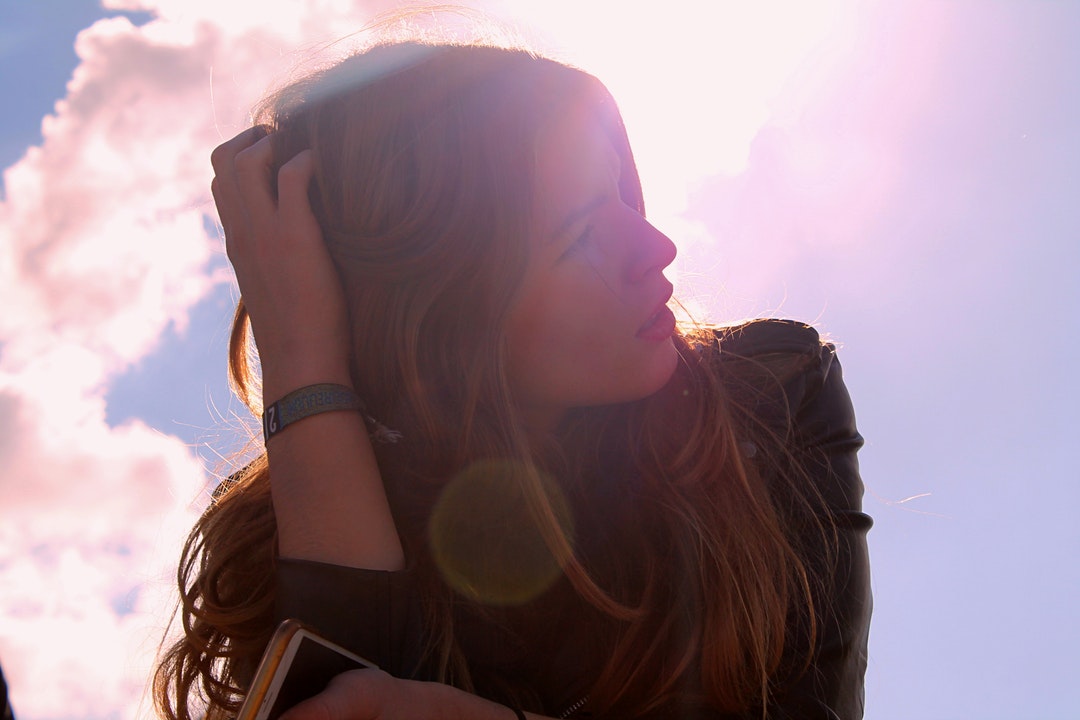 Portrait of a young woman in a leather jacket, posing with clouds in the background.