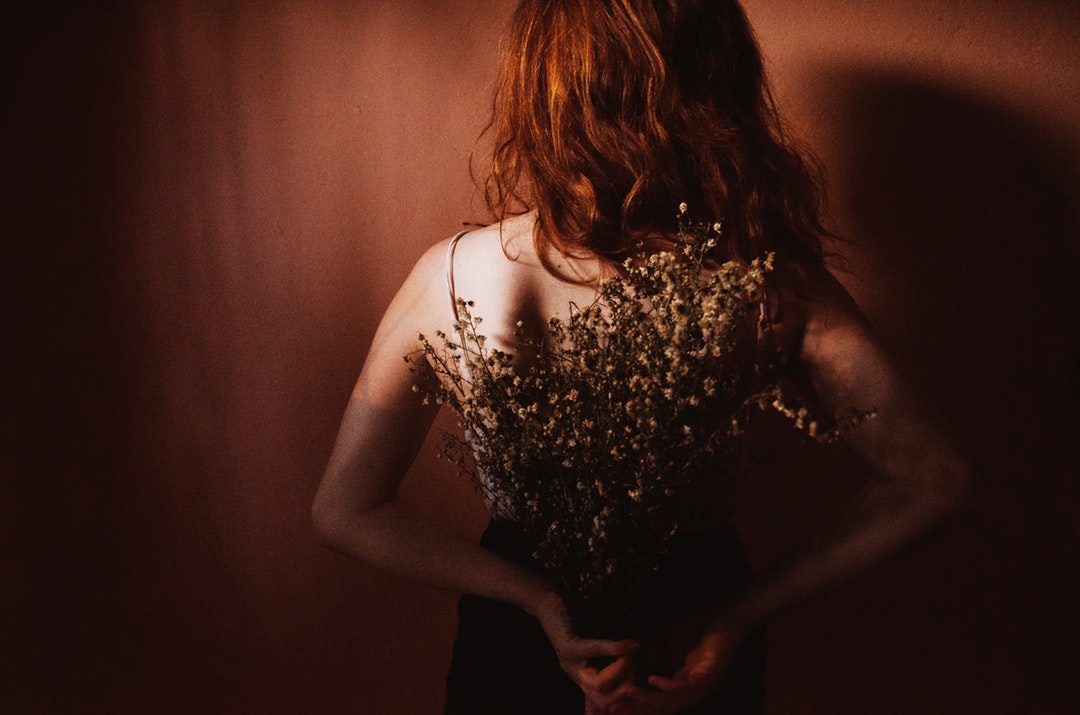 Woman holding a bouquet of dried flowers behind her back in a red shadowed room