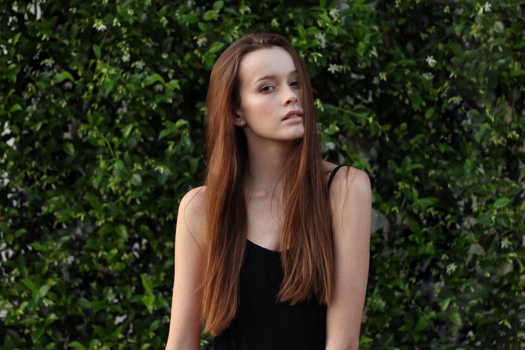 A young brunette woman posing near a hedge