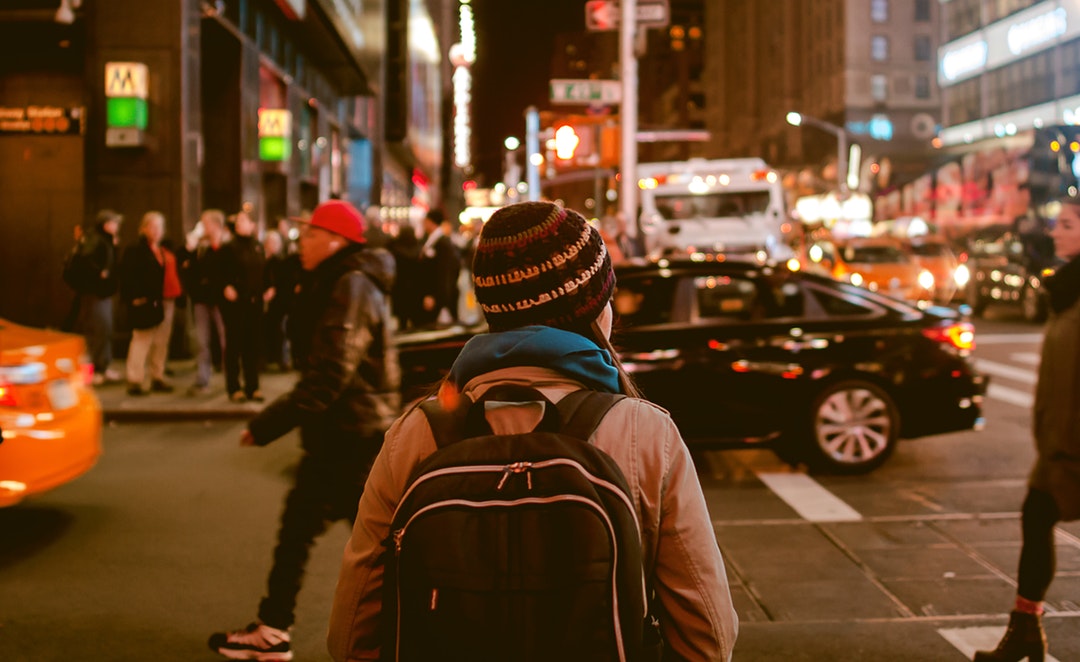 A backpacker in a knit cap in the streets of New York at night
