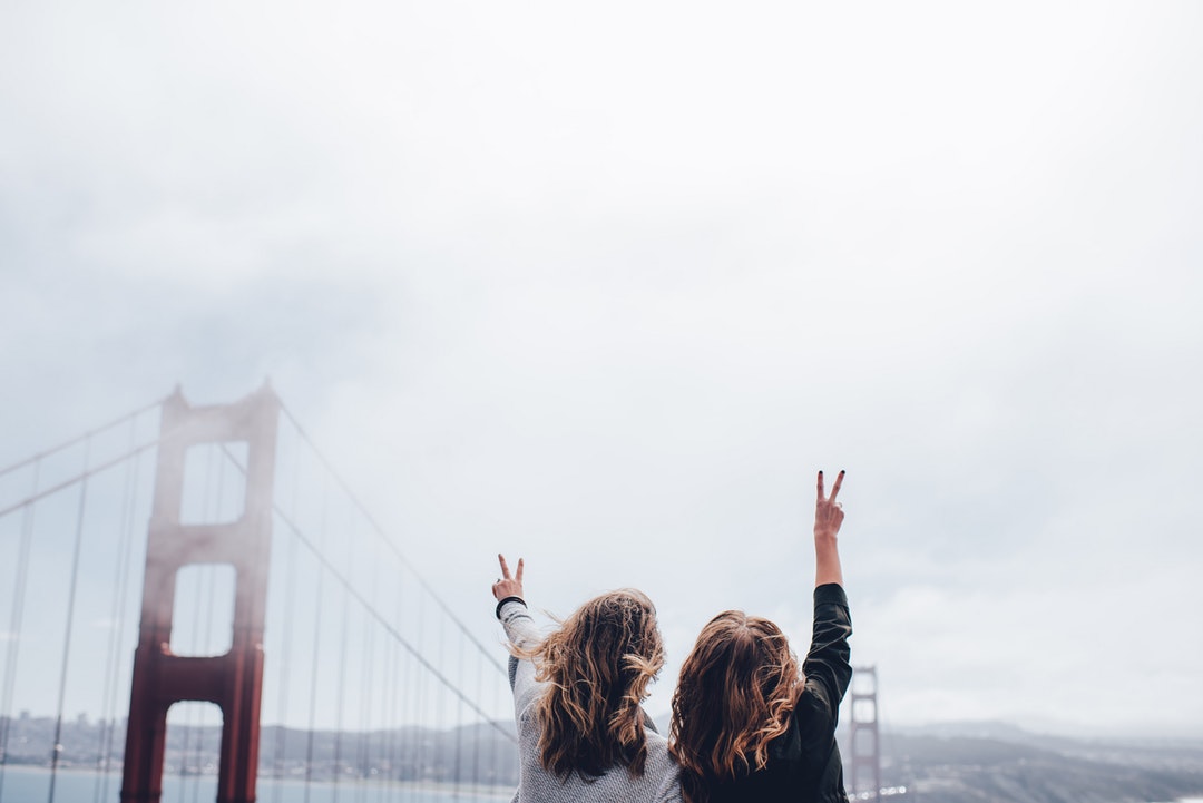 Two women giving the V gesture near San Francisco's Golden Gate Bridge