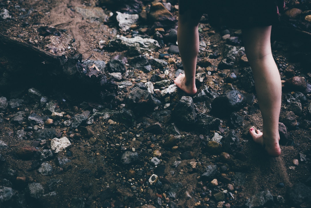 A barefoot girl walking over stones