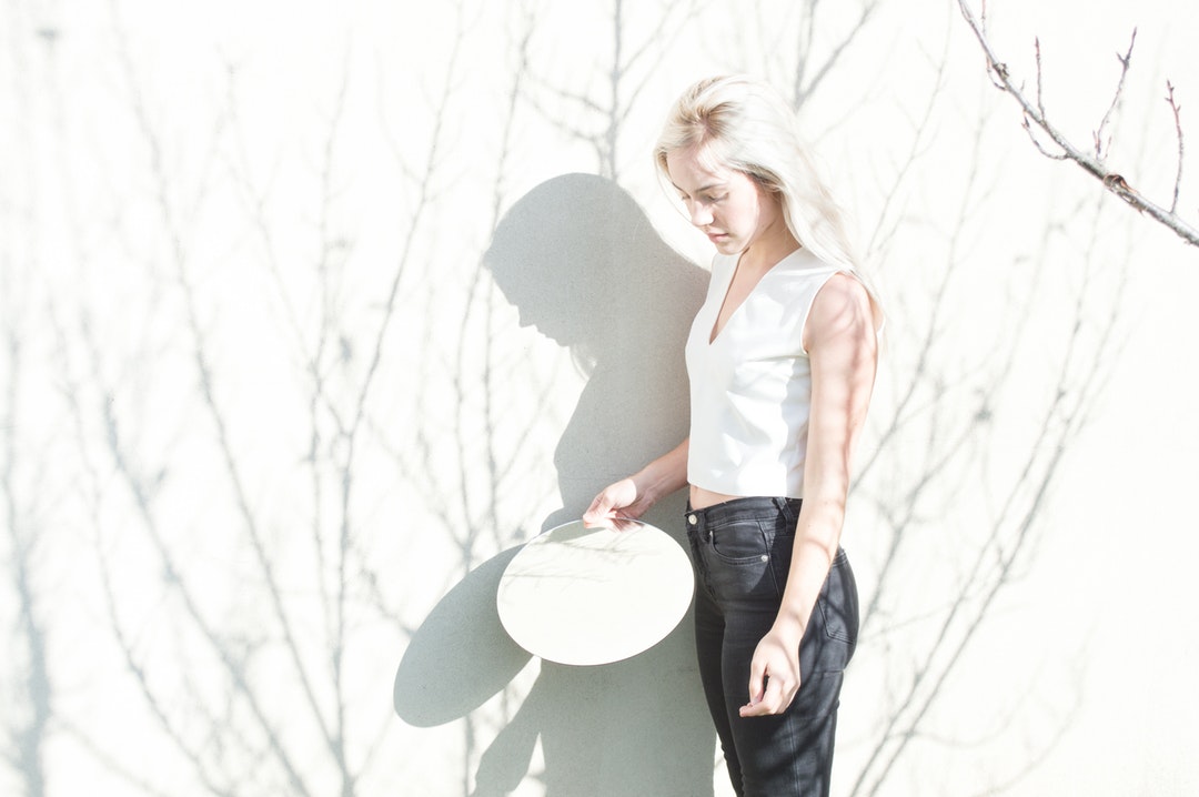 Woman in overexposed light holidng a circle mirror