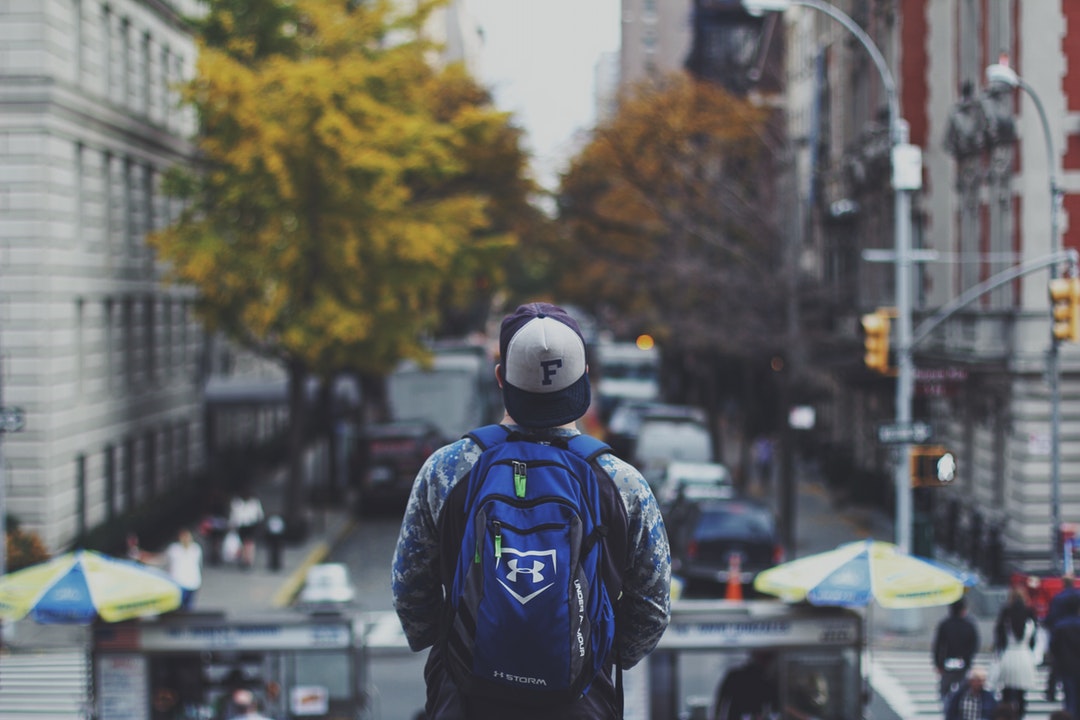 A man in a cap and a backpack looking at a busy street in New York.