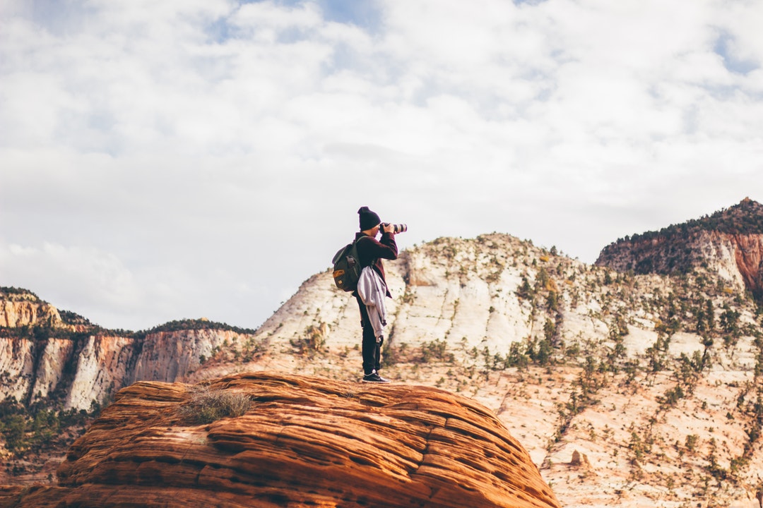 Person on a cliff using a camera to photograph mountains