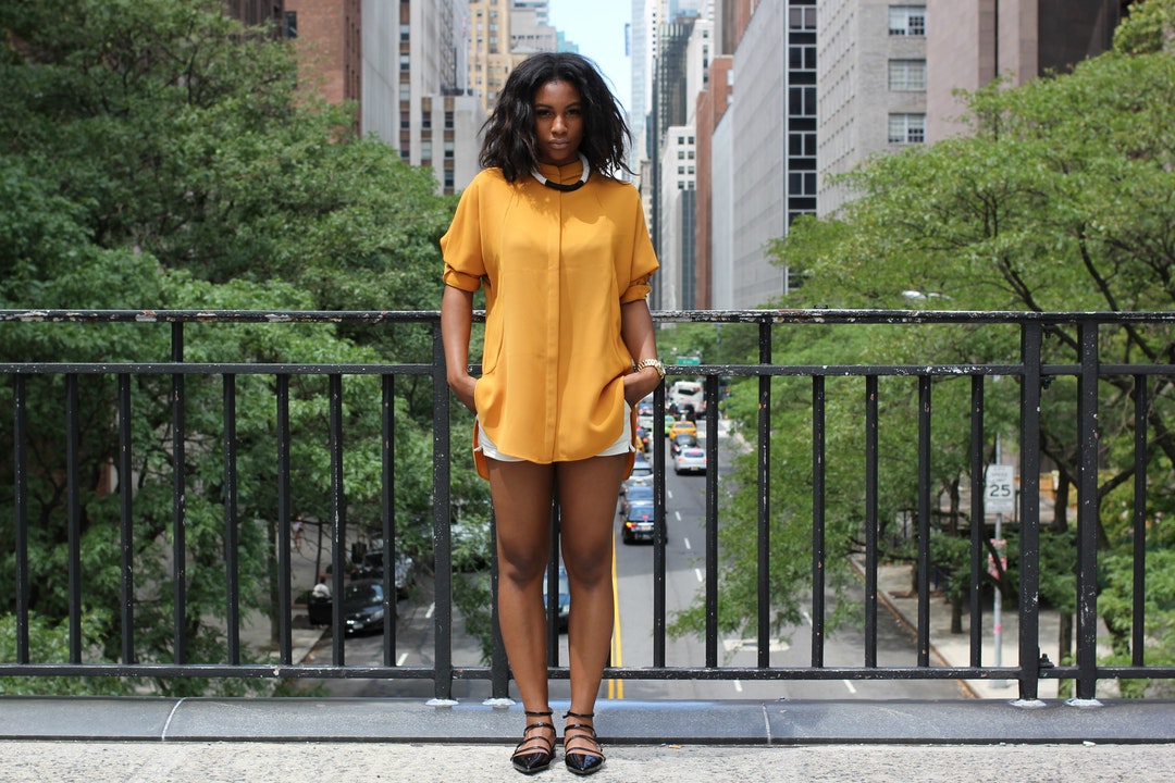 Woman models a yellow shirt and shorts on a bridge in New York