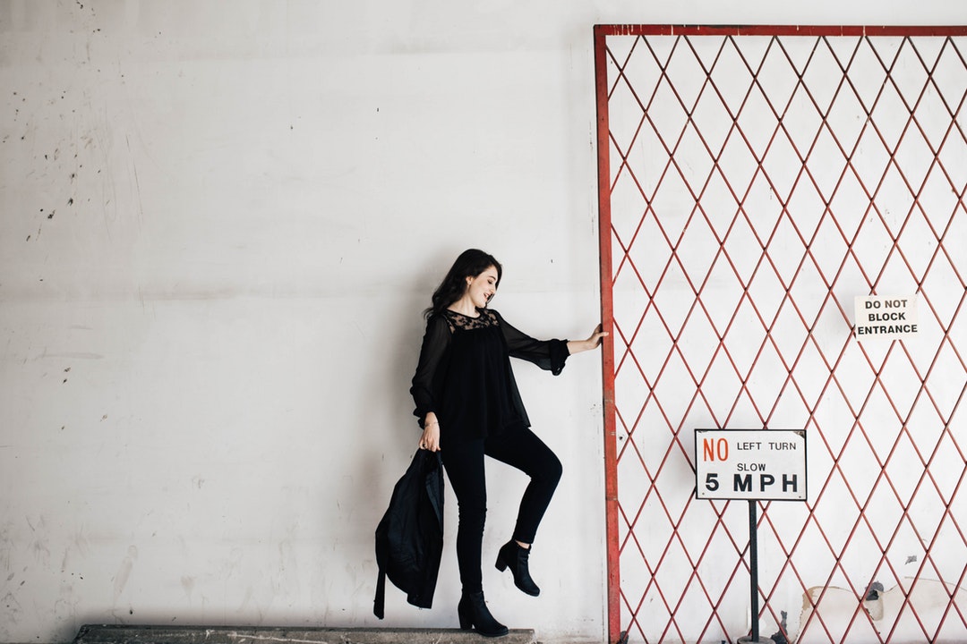 A woman dressed in black is holding onto the entrance gate next to the signs.