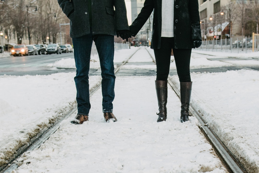 On train tracks covered in snow, two lovers stand holding hands
