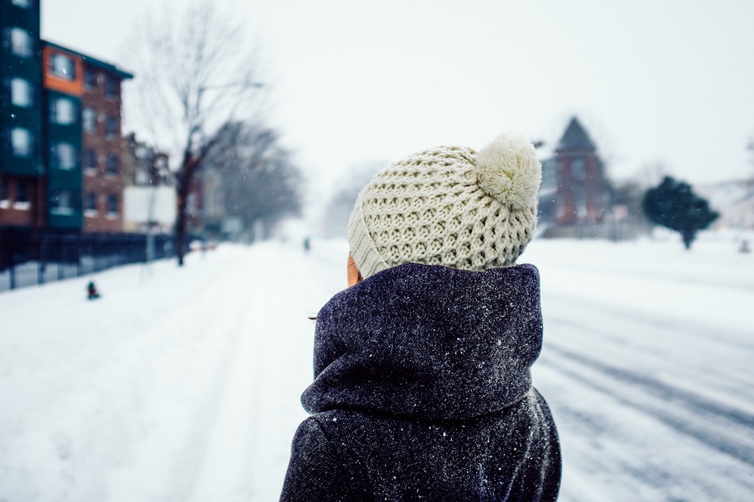 Person wearing a winter hat and coat standing in a snowy street