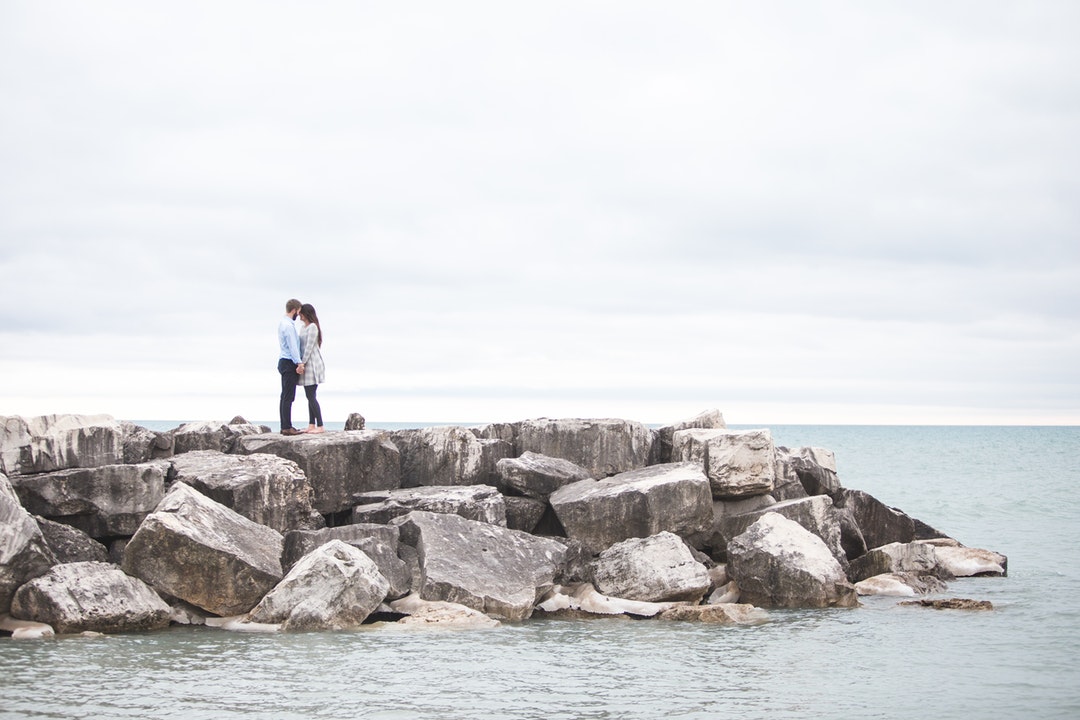 Standing on a stone jetty on the ocean, a couple shares a tender moment