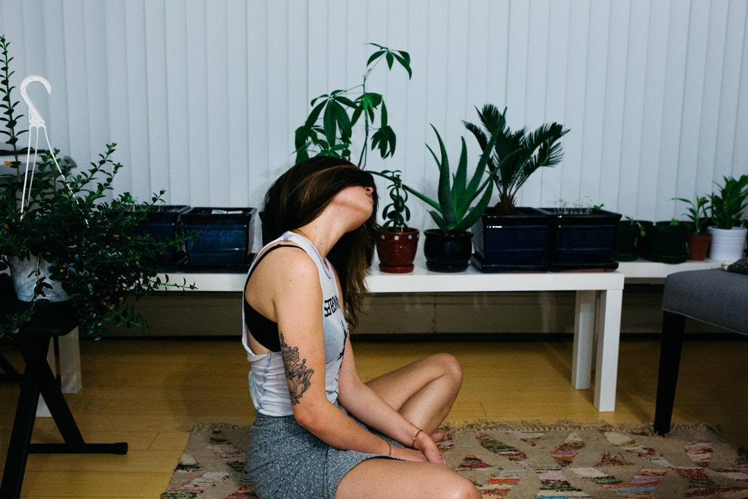 A brunette woman doing yoga in her living room that is filled with plants