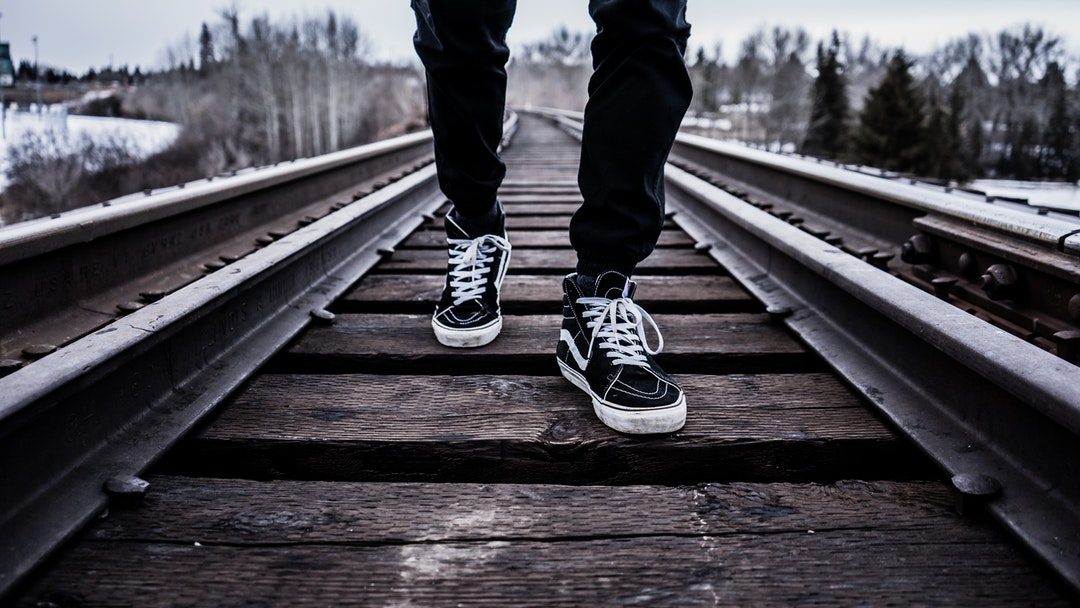 A person's feet in sneakers on a railroad track