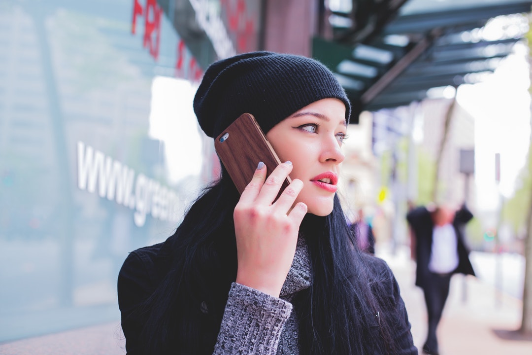 A young woman in a beanie talking on a phone while standing on a sidewalk