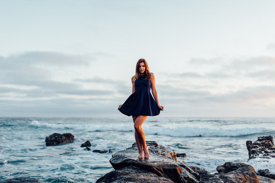 Woman in a dress posing on the shoreline rock at Windansea Beach