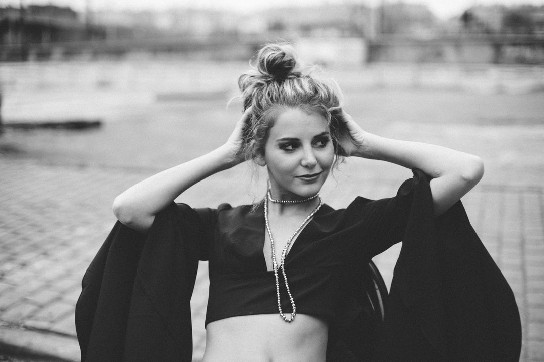 Black and white shot of young attractive girl with hair bun and fashionable clothes smiling