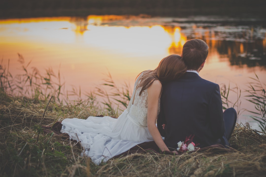 Bride rests head on groom while looking at a pond during sunset