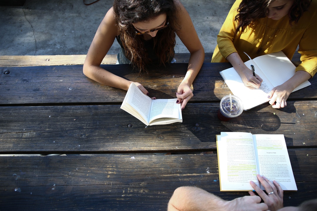 Three people reading and taking notes at an old wooden table outdoors