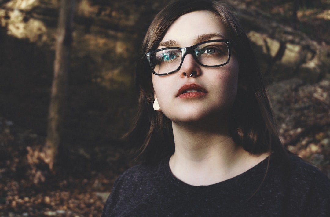 Trendy young woman with a nose ring and glasses looks up