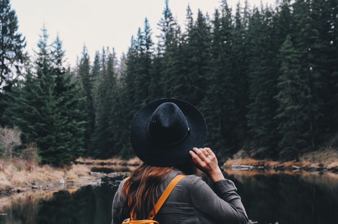 A woman in a black hat is facing the river and forest in Mactaggart Sanctuary.