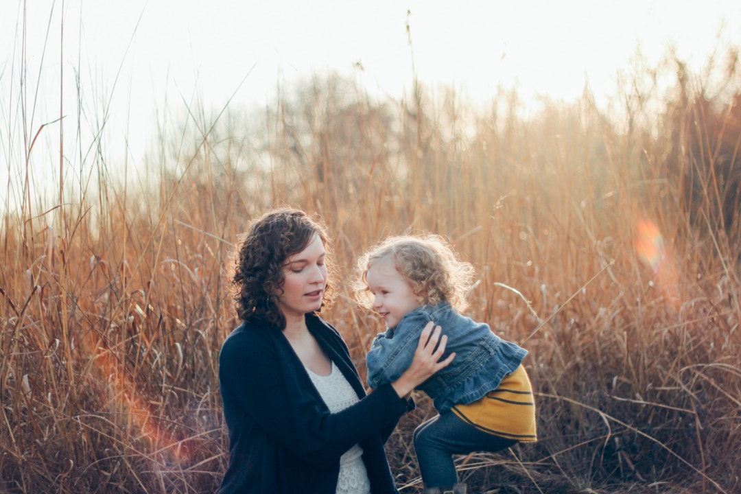 Woman about to carry a happy toddler in a meadow in Illinois with the sun shining