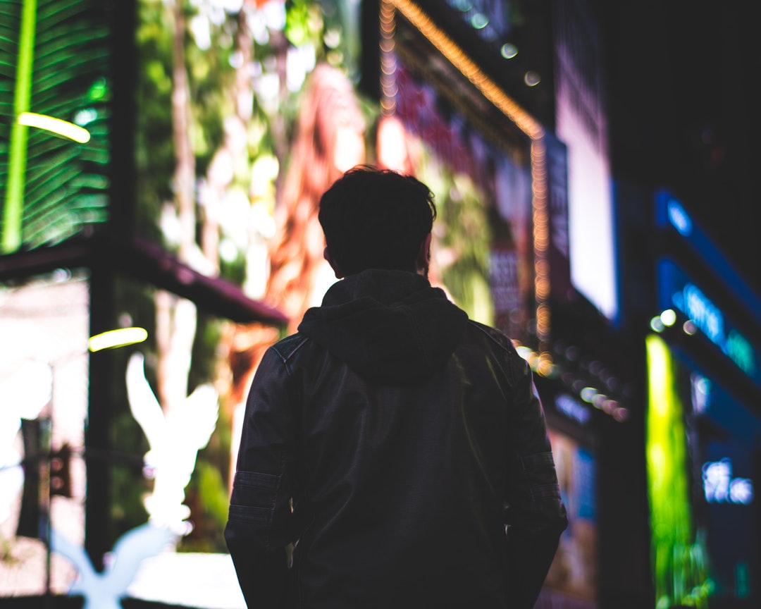 Man in a jacket crossing the street in front of bright New York City lights