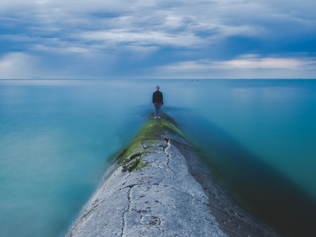 A man standing on a barrier just above the sea in Phare des Baleines