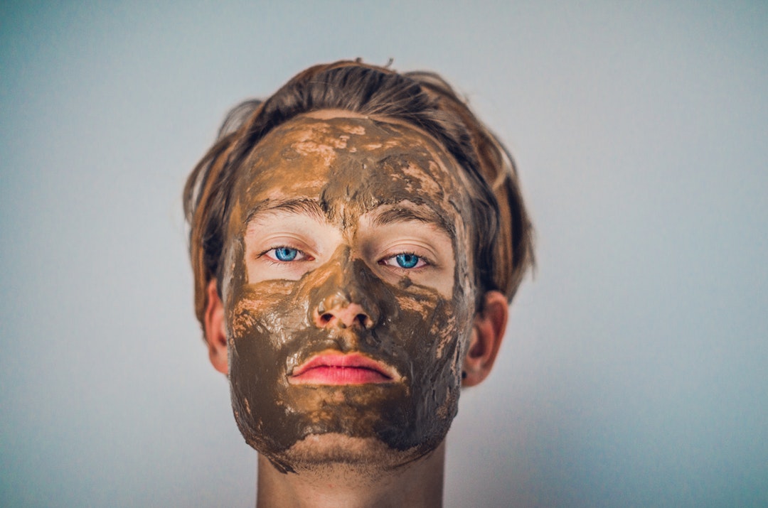 A blue-eyed man with a mud mask on his face