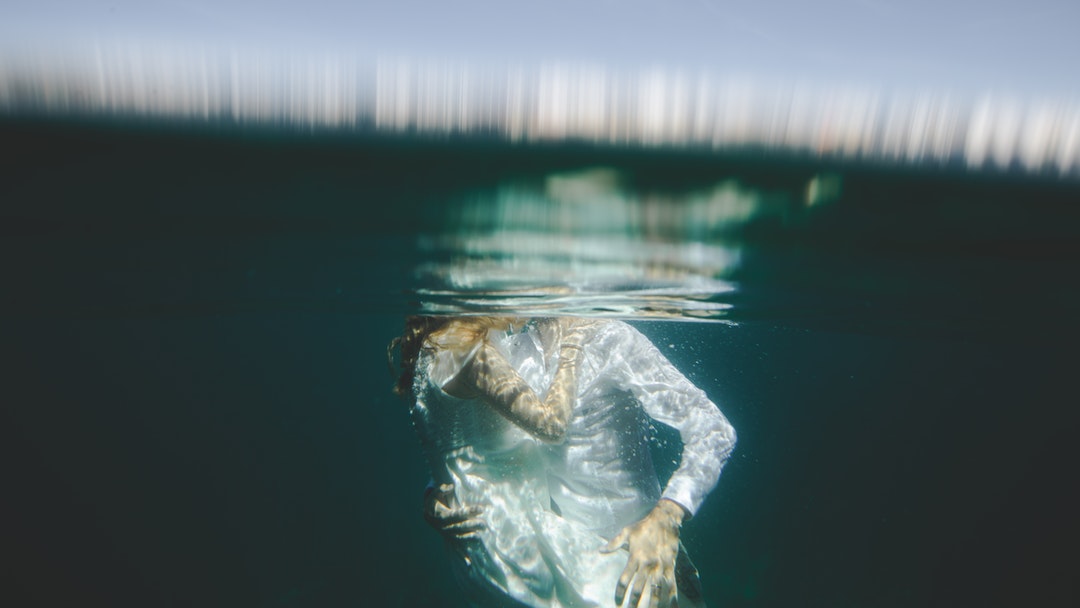 Underwater photo of a bride and groom plunged below the surface, sharing a kiss