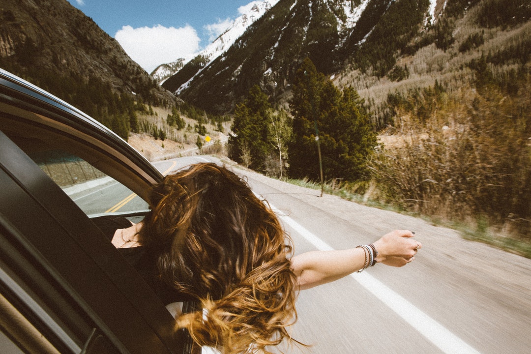 Young woman leans out car window to feel the fresh mountain air
