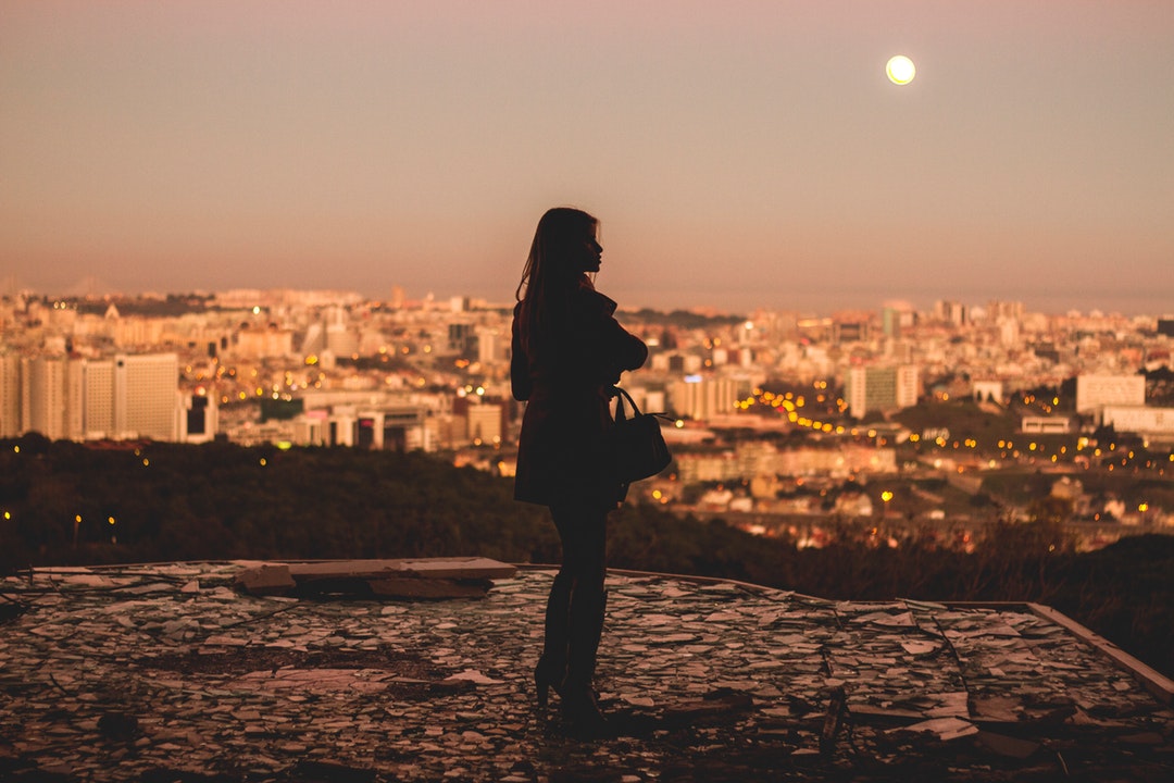 The silhouette of a woman looking across the cityscape of Lisbon during sunset.