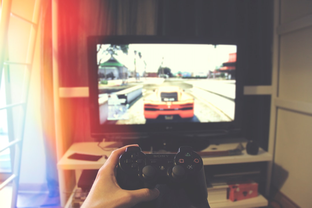 Person holding PS3 game controller and playing Grand Theft Auto on television under bunk bed