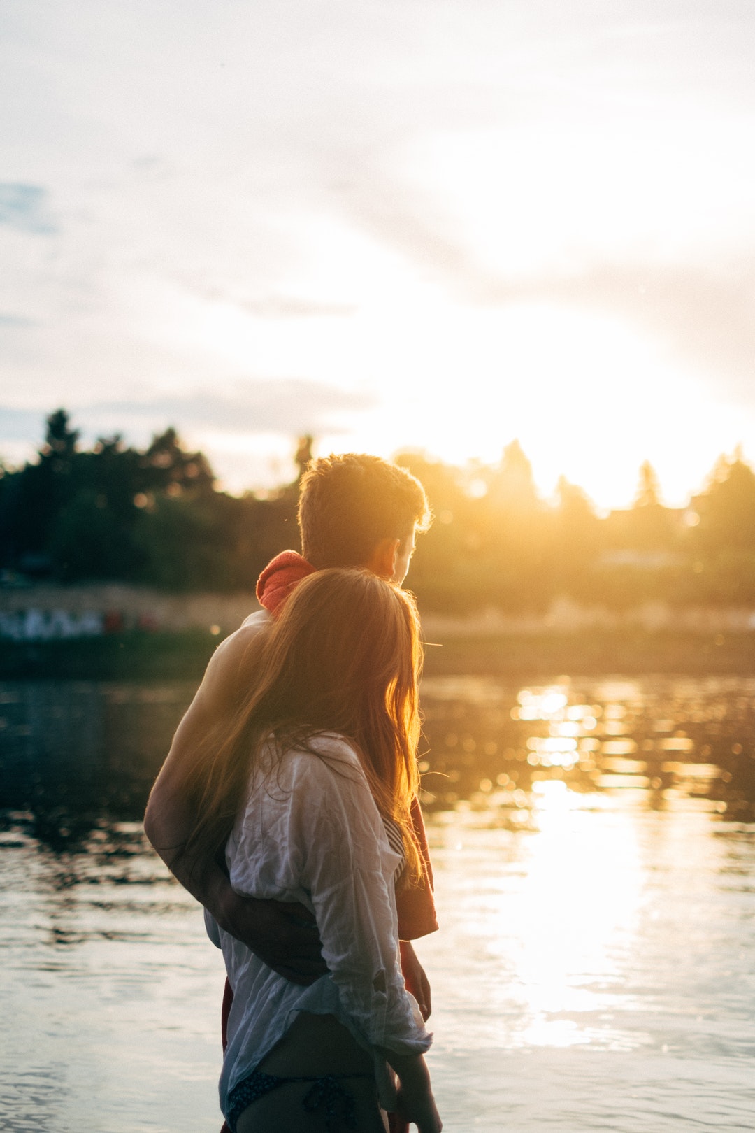 A couple stands by a lake in the sunshine in Dresden. His arm is around her.