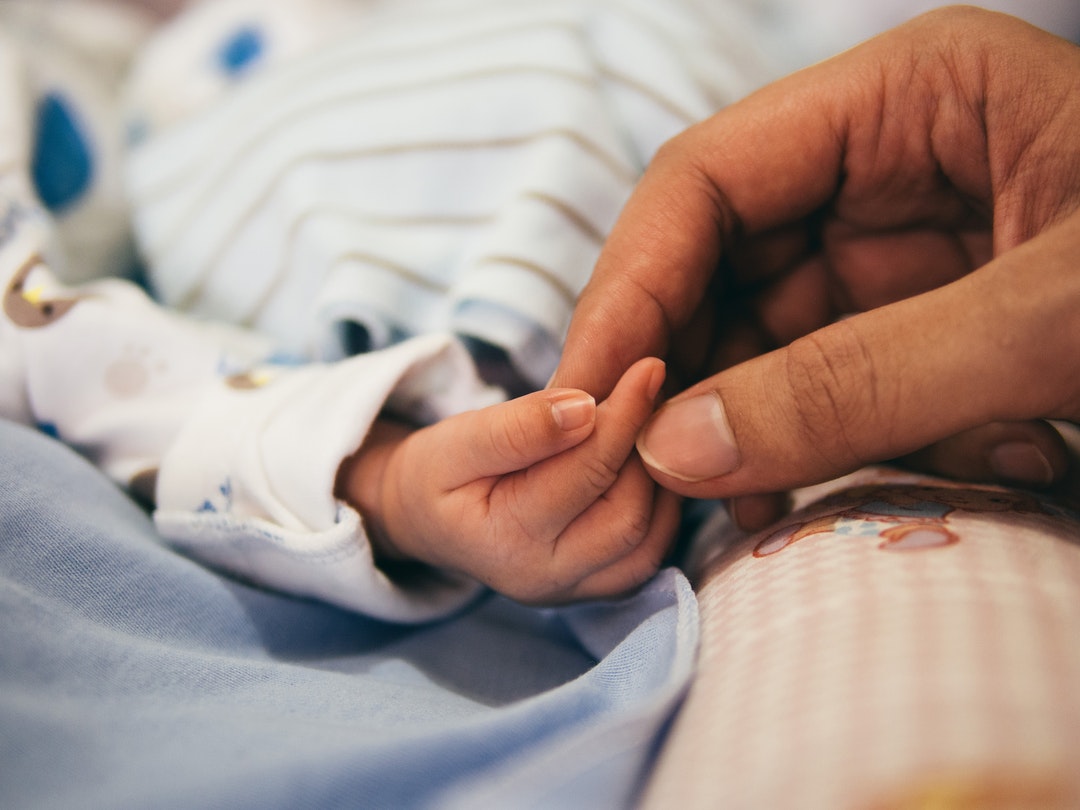 A parent holds a sleeping baby's tiny hand