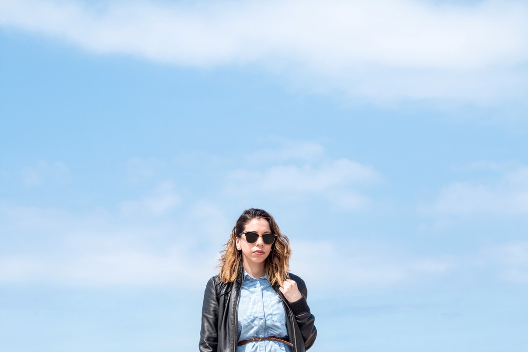 Woman in black leather jacket and sunglasses posing in front of blue skies at Santa Monica State Beach