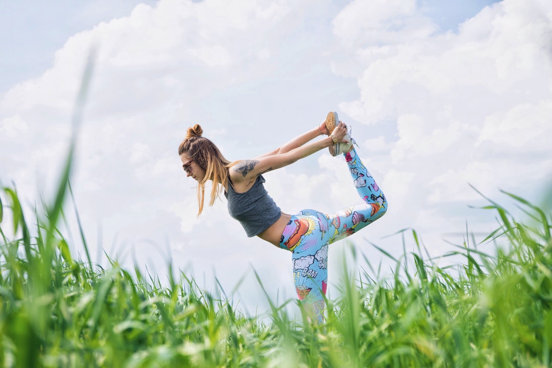 A woman wearing funky leggings doing yoga on the grass in Karczewski