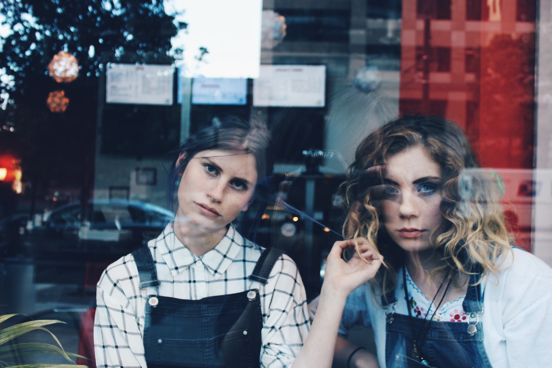 Two young women stare angrily out a reflective window