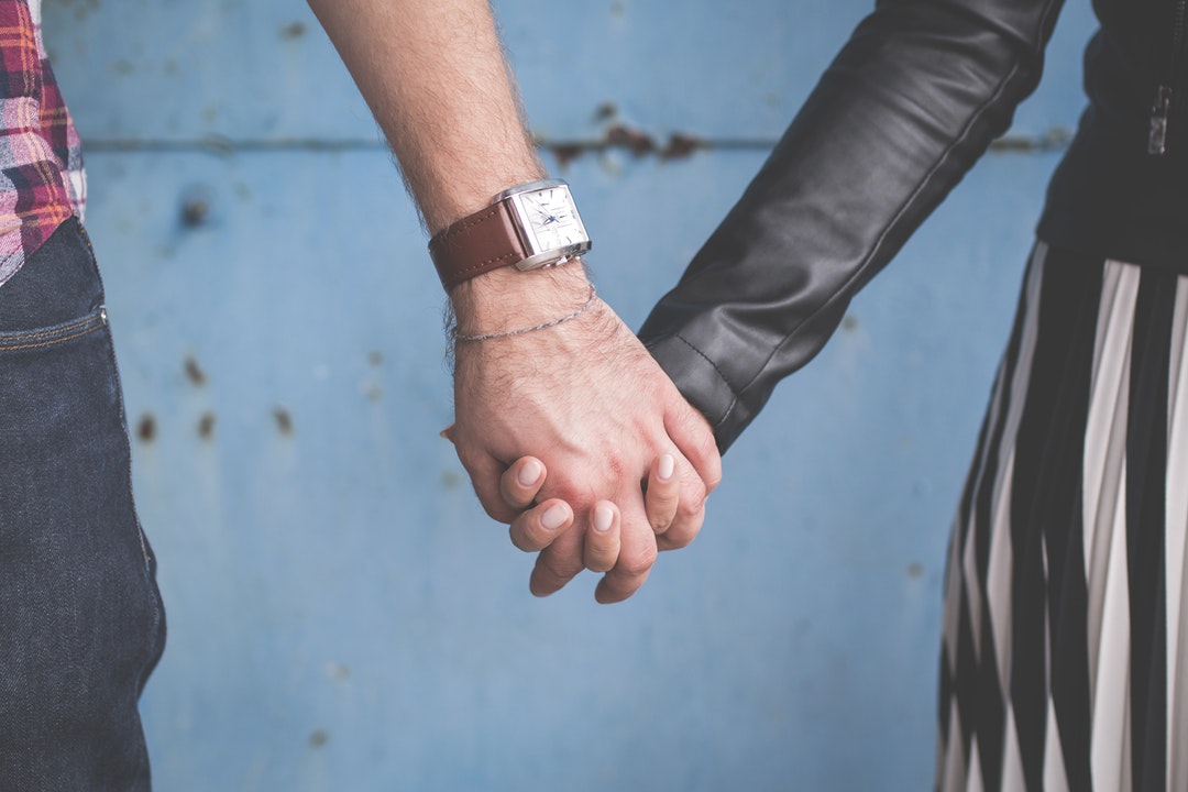 A couple links fingers in front of a blue wall in Olsztyn