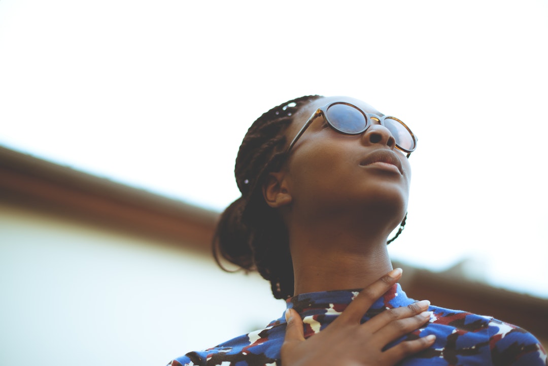 A fashionable young woman in sunglasses and a colorful shirt looking away from a camera.