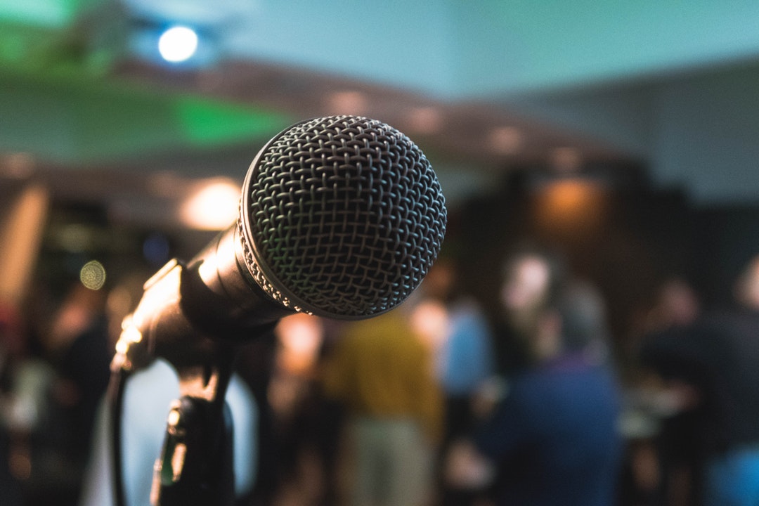 A close-up of a microphone with a group of people in the blurred background