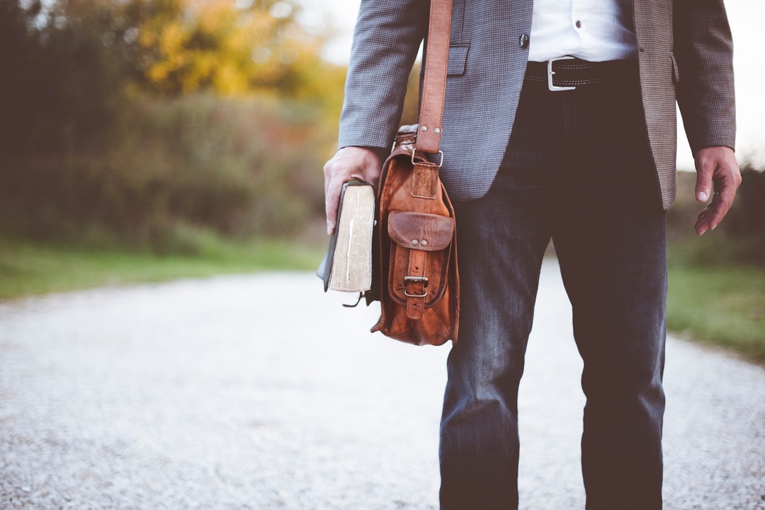 A low shot of an elegantly dressed man with a leather bag holding a book in his hand
