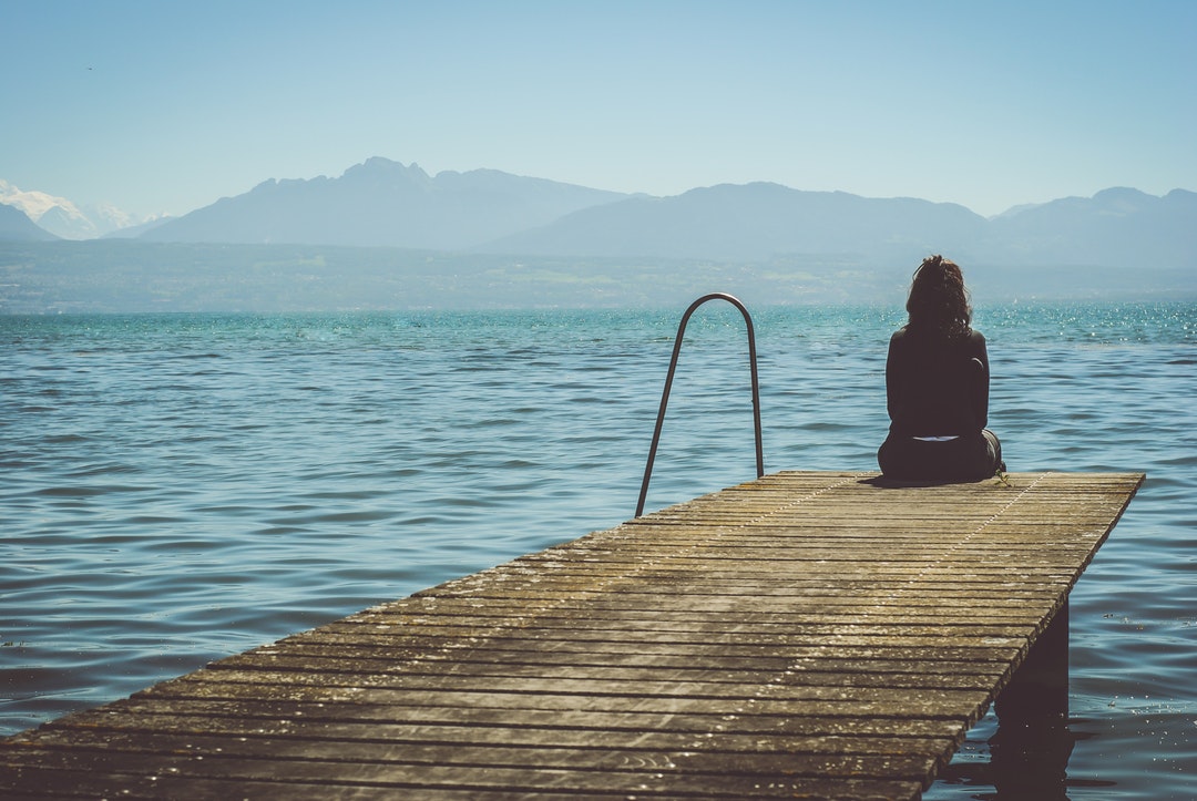 A girl in Morges sits at the end of a dock and stares at the mountains