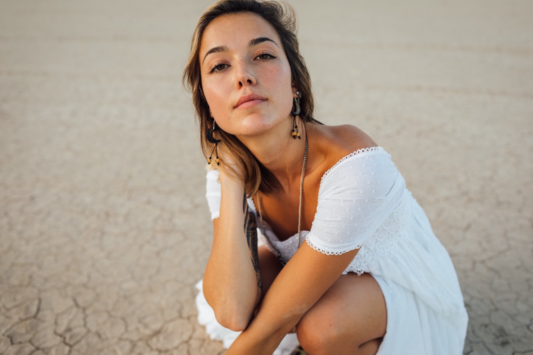 Woman in a white dress crouched down in the desert