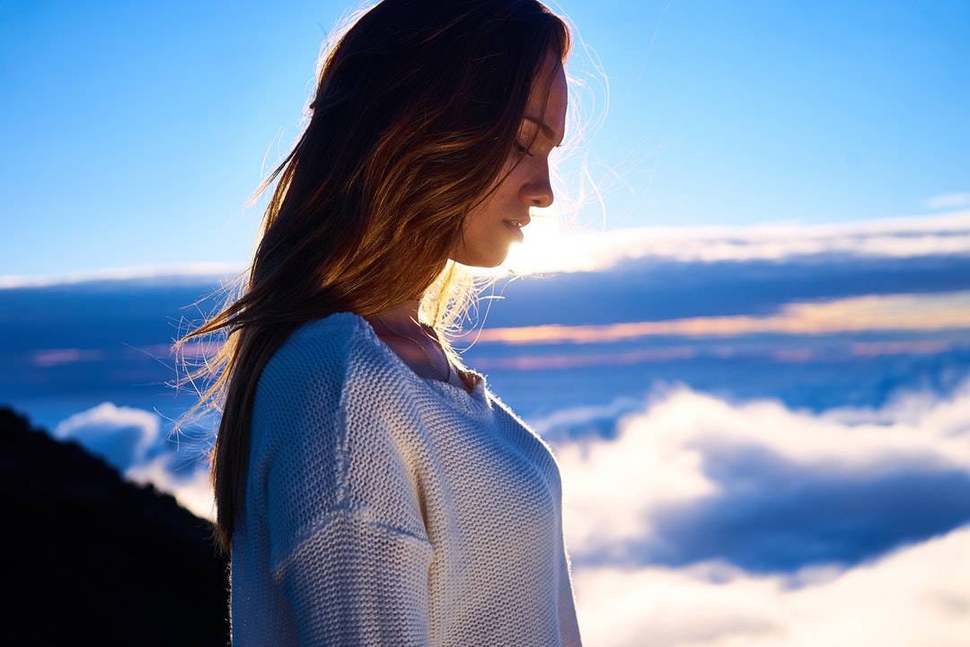 Woman with long hair and sweater at a high altitude looking down during sunset in Route du Volcan