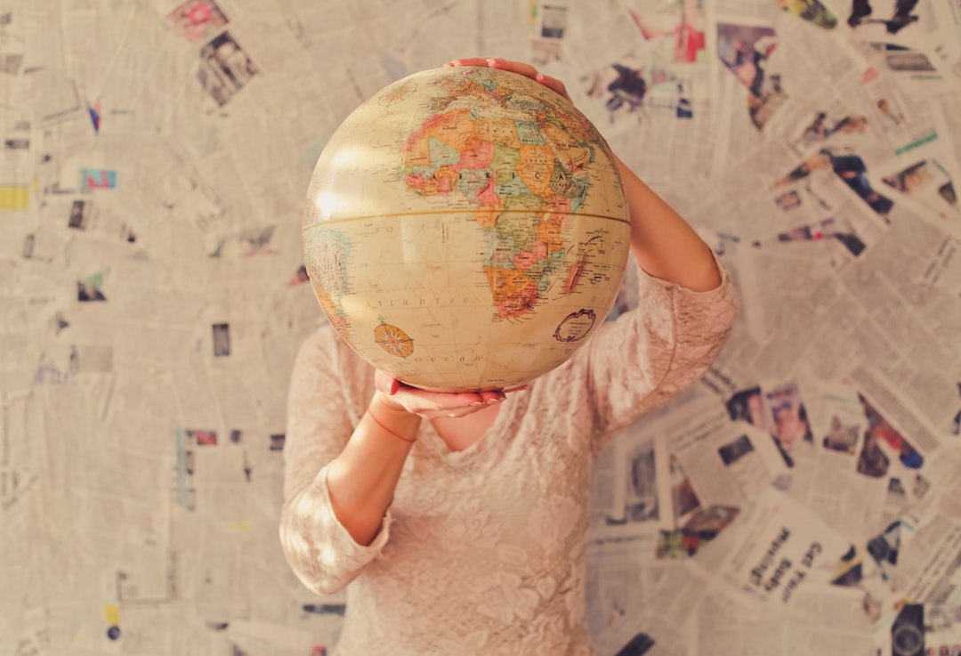 A woman in a lace blouse holding up a globe in front of her head