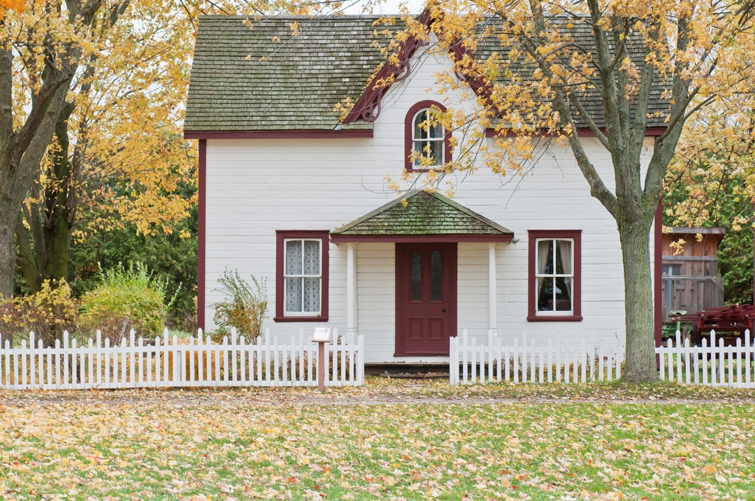 A small white house surrounded by trees in the autumn