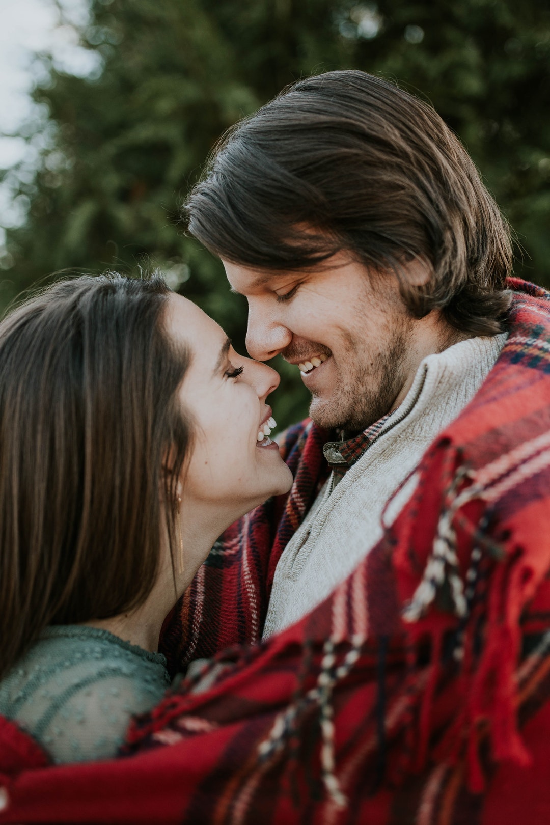 Man and woman wrapped together in a red plaid blanket outdoors
