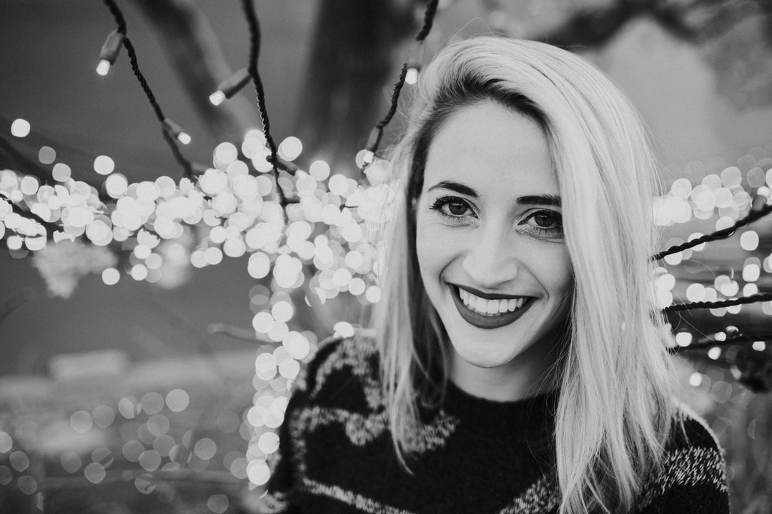Happy young woman smiles among strings of Christmas lights