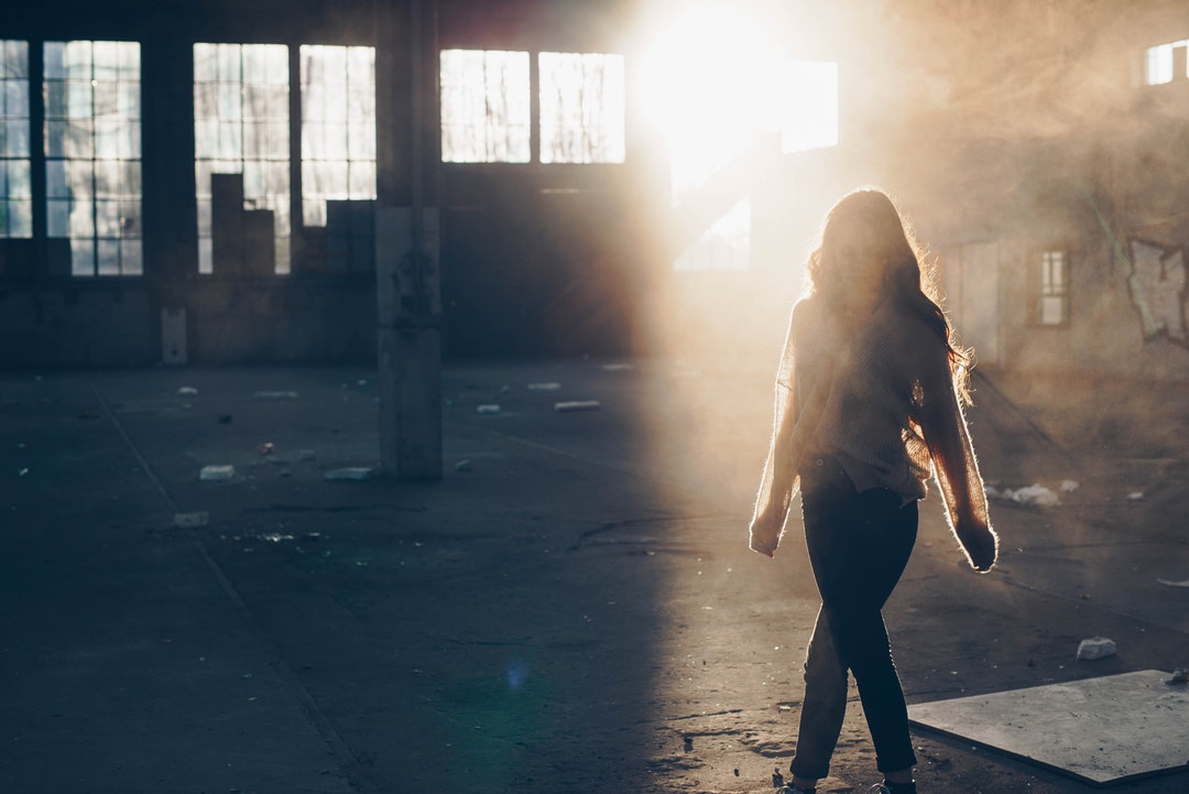Backlit woman walks through an abandoned foggy warehouse